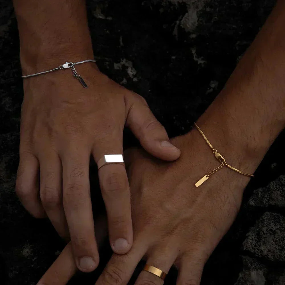 Silver-tone snake chain bracelet on the wrist, styled with rings and a second bracelet