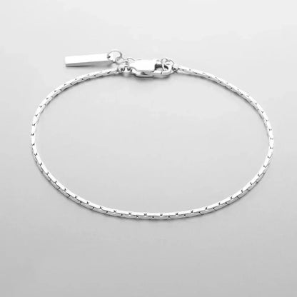 Fine bar link chain bracelet laid out on a gray background